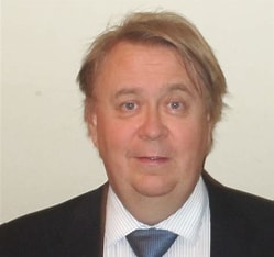 Portrait of a middle-aged man with light hair wearing a dark suit and blue tie, facing the camera.